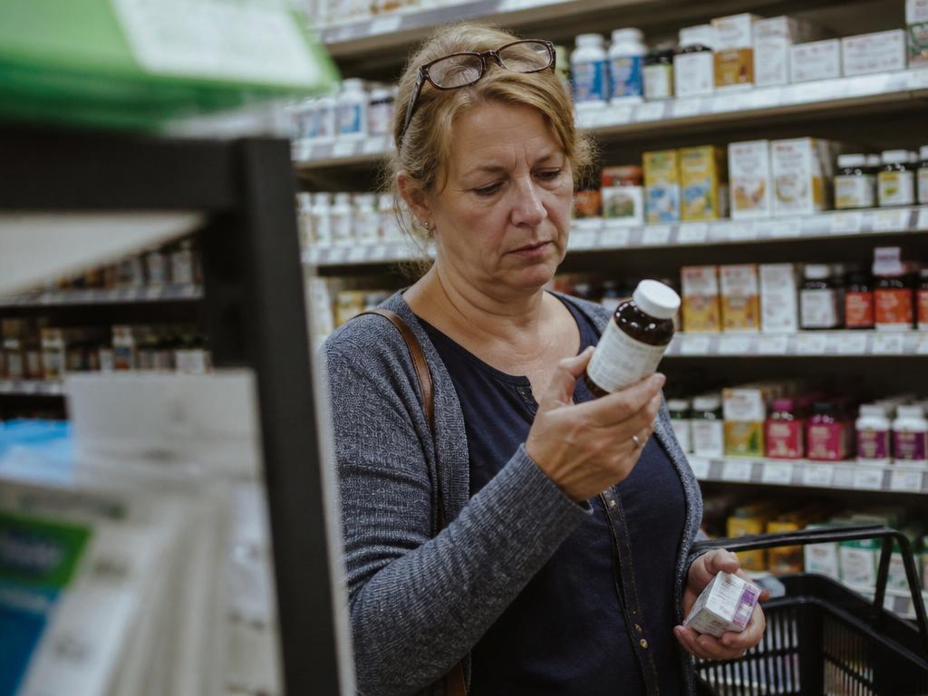 A woman reading the label on a supplement bottle in a pharmacy aisle